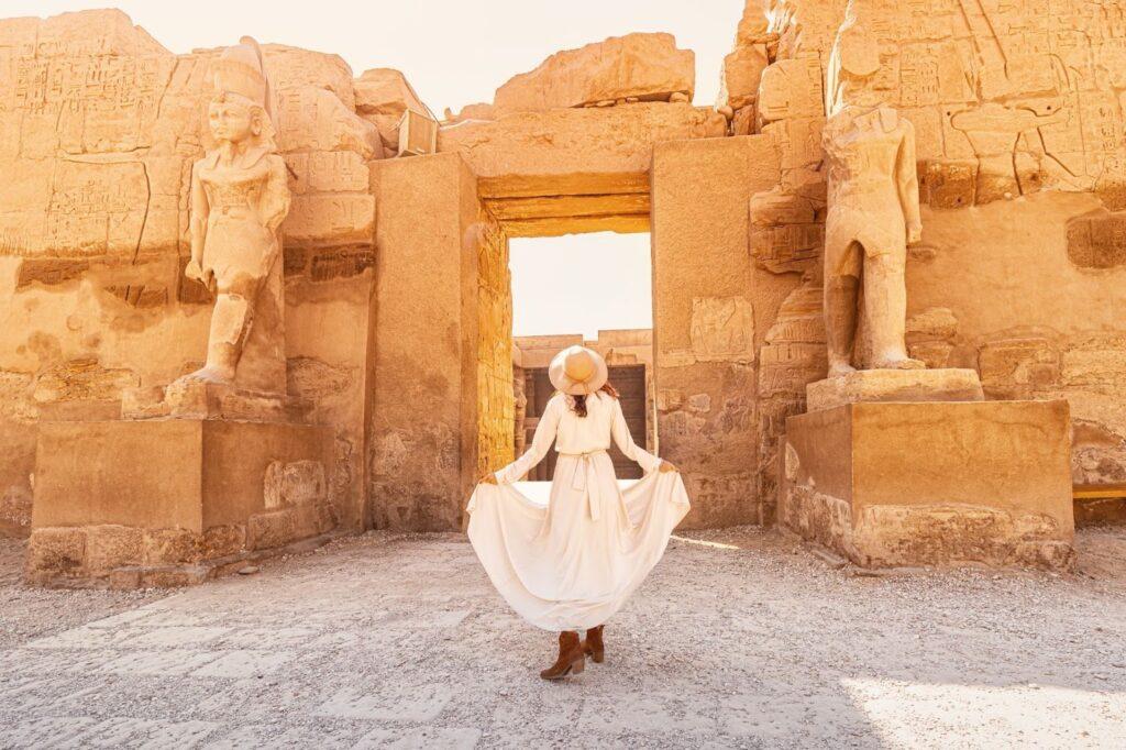 Happy woman traveller explores the ruins of the ancient Karnak town in the heritage city of Luxor or Thebes in Egypt. Entrance to the Ramesses III Temple