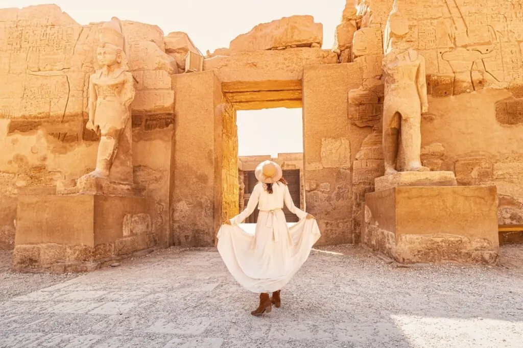 Happy woman traveller explores the ruins of the ancient Karnak town in the heritage city of Luxor or Thebes in Egypt. Entrance to the Ramesses III Temple
