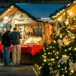 Unidentified people stand near illuminated wooden kiosk with souvenirs at traditional christmas market as christmas tree with lights in foreground in Asti, Italy