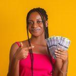 young woman with braided hair and a pink top, smiling as she holds a fan of Botswana Pula banknotes
